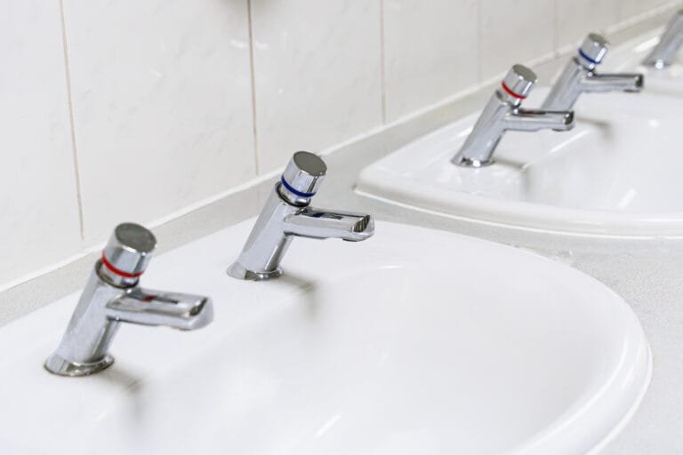 Chrome separated hot and cold water taps, manual water mixing in public restroom in UK.